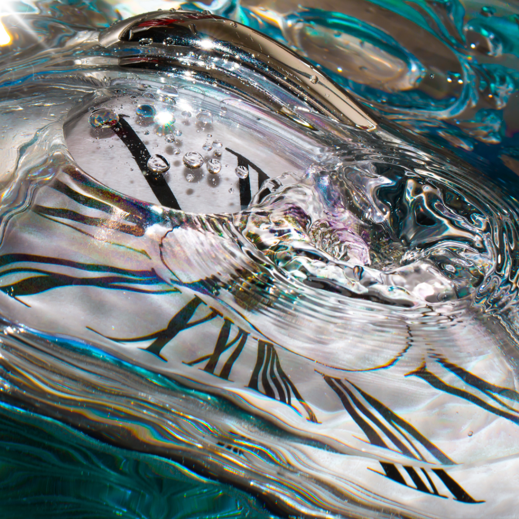 Image of pocket watch under water with drop of water causing ripple on surface so image is distorted
