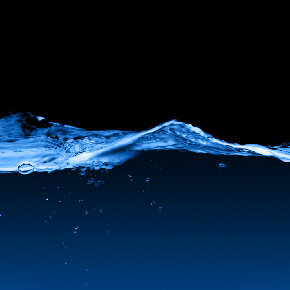 Image of dark blue water with a rippling wave and bubbles beneath the surface.