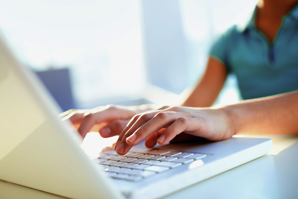 Photo of a person's hands typing on a white laptop keyboard in bright light.