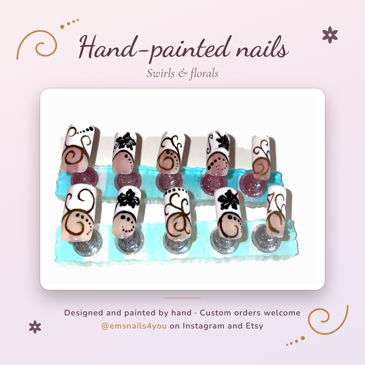 Ten hand-painted press-on nails on display stands, with white tips decorated with gold swirls, dotted lines and black flowers, framed on a soft pink card reading Hand-painted nails, @emsnails4you