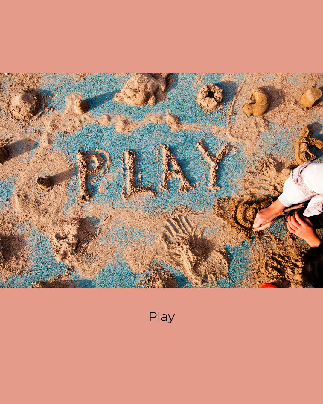 The word Play drawn in sand over blue ground, surrounded by sand shapes, with a child's hands digging at the edge. Caption: Play.